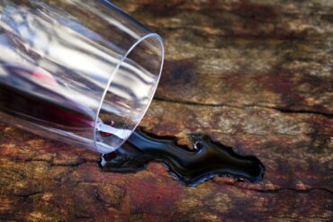 Aus umgefallen Glas läuft Rotwein auf Holztisch